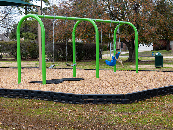 Swing set with inclusive seating and engineered wood fiber mulch contained by ADA-compliant borders.