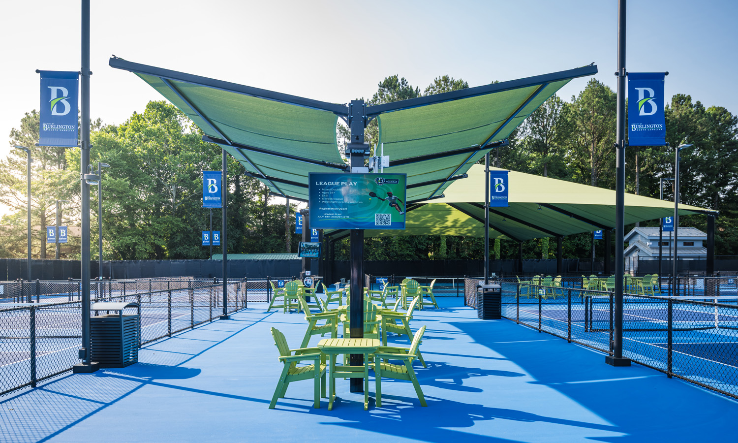 League play information screen displayed under shaded seating area at Burlington Pickleball courts.