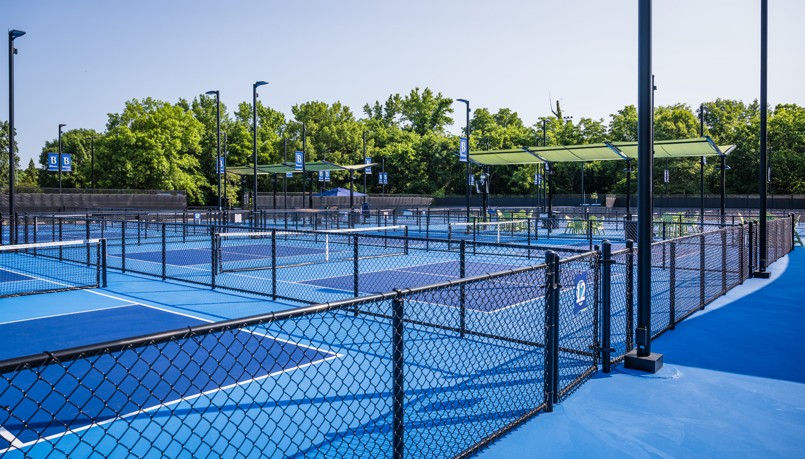 Fenced pickleball courts at Burlington recreation facility with shaded rest areas.