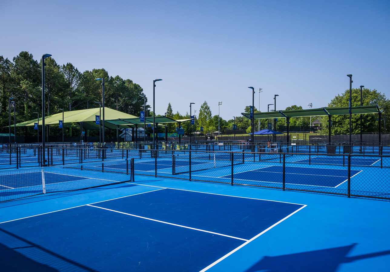 Wide view of multiple blue pickleball courts with shade canopies and seating areas.