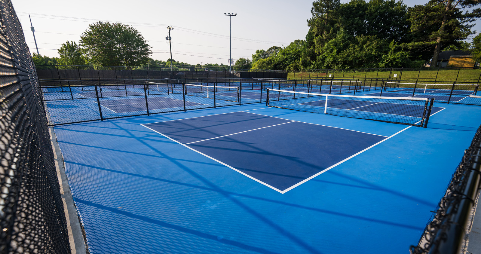 Close-up of blue pickleball courts surrounded by fencing at Fairchild Pickleball & Tennis in Burlington, NC.