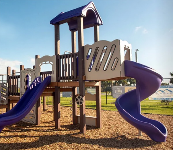 Outdoor playground featuring a purple spiral slide, straight slides, and mulch safety surfacing.