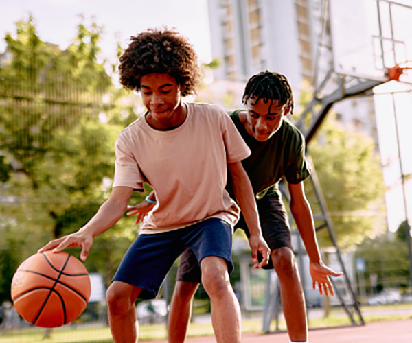 Young man shooting a basketball on a community court with leafless trees in the background.