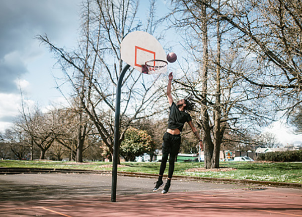 Red and blue rubberized outdoor basketball court with adjustable hoop and surrounding fencing.