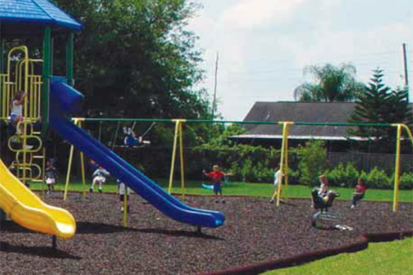 Children playing on a colorful playground with mulch safety surfacing and multiple swing sets.