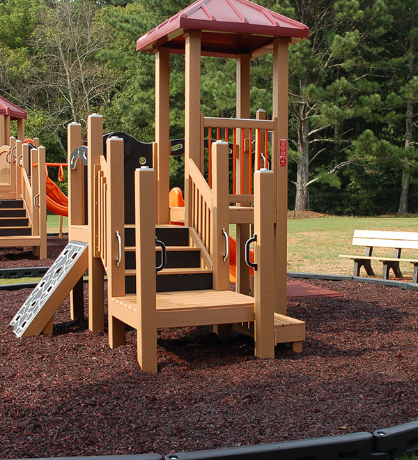 Inclusive playground with composite decking and rubber mulch surface under shaded play equipment.