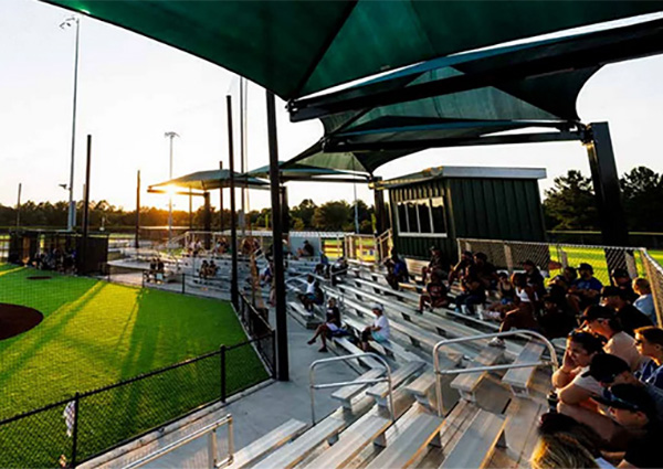Covered aluminum bleachers at a baseball field with fans at sunset by Superior Recreation of the Carolinas.