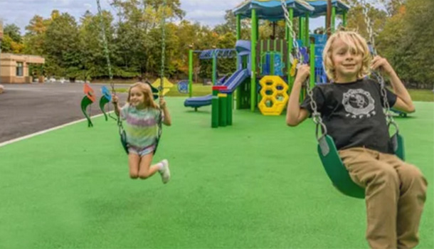 Kids swinging on modern playground equipment with bright green turf at local recreation park.